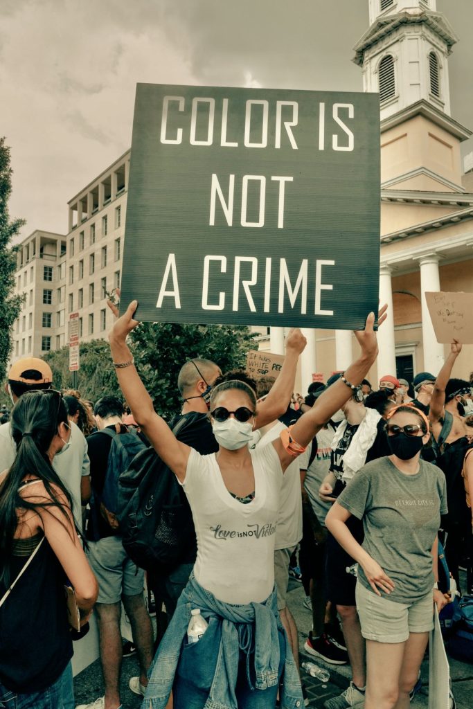 Image of a protester holding a sign that says "color is not a crime."